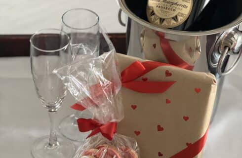 Bottle of Santa Margherita Prosecco on ice - Varmont Chocolates from Mother Myrick's wrapped in decorative valnetine paper and a bag of Leslie Hall's Sweetie Pies cookies.