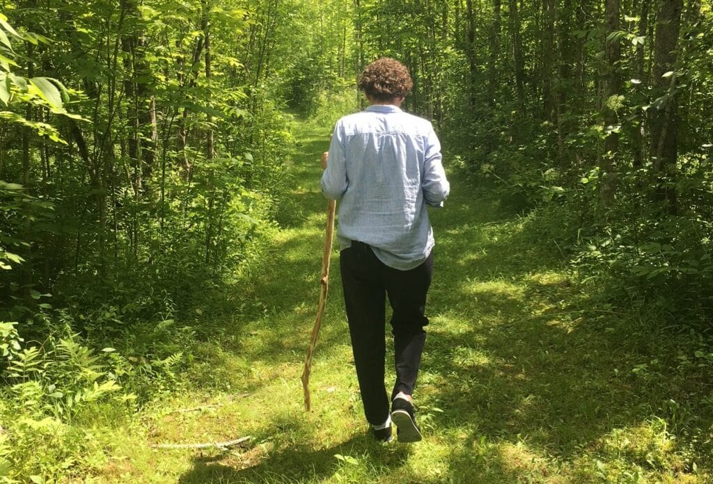 Woman walking through forest with walking stick