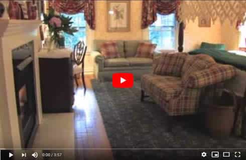 Video Thumbnail of a guestroom with a bed, two sofas and a fireplace.