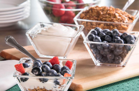 Bowls full of ingredients for yogurt parfait with strawberries, blueberries and granola.