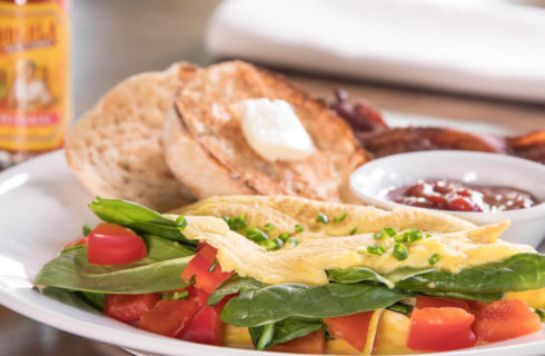 Omelet with spinach and tomatoes on a white plate with an english muffin and bacon.