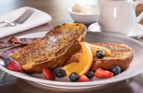 French toast garnished with orange slices and berries on a white plate with coffee in a white mug.