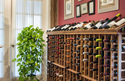 A wooden wine rack full of many bottles of wine next to a set of white french doors.