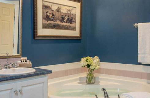 Bathroom with a cabinet vanity, mirror, corner soaking tub and blue walls.