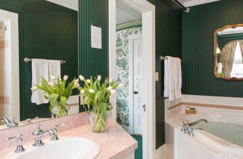 Green striped wallpaper in a bathroom with a pink vanity and a large soaking tub.