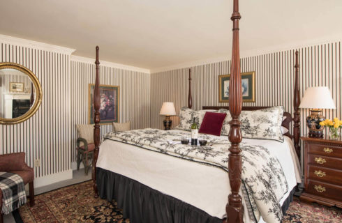 Large guestroom with black and white wallpaper and bed coverings and colonial style cherry furniture.