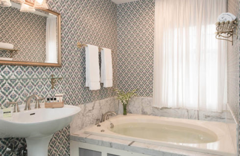 Bathroom with pedestal sink, soaking tub and blue patterned wallpaper.