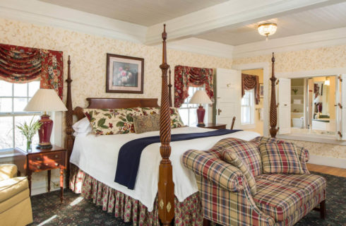 Large bright bedroom with a tall four-post bed, a plaid sofa and two large windows.