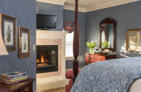 Bedroom with blue wallpaper, a four-post bed and fireplace with a TV above it.