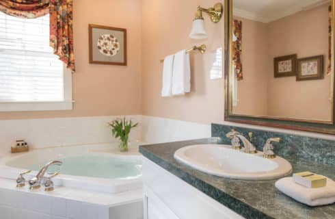 Bright and clean bathroom with a large soaking tub and a cabinet sink in white with a green counter.