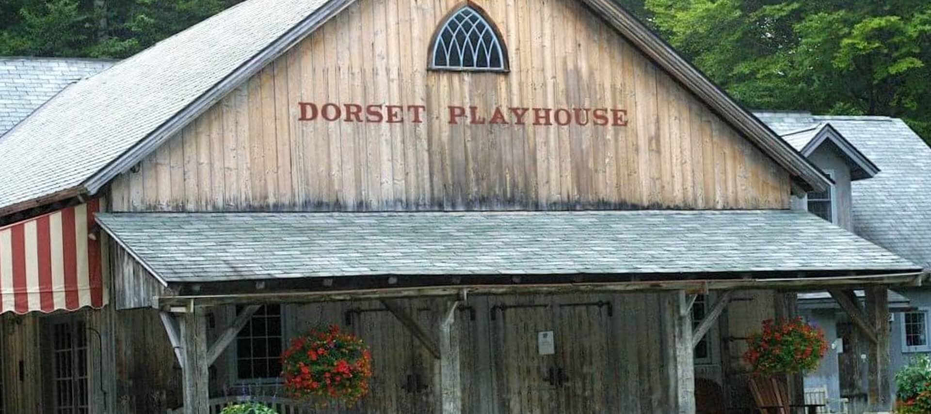 Large wooden building with red striped awnings and a sign that says Dorset Playhouse.