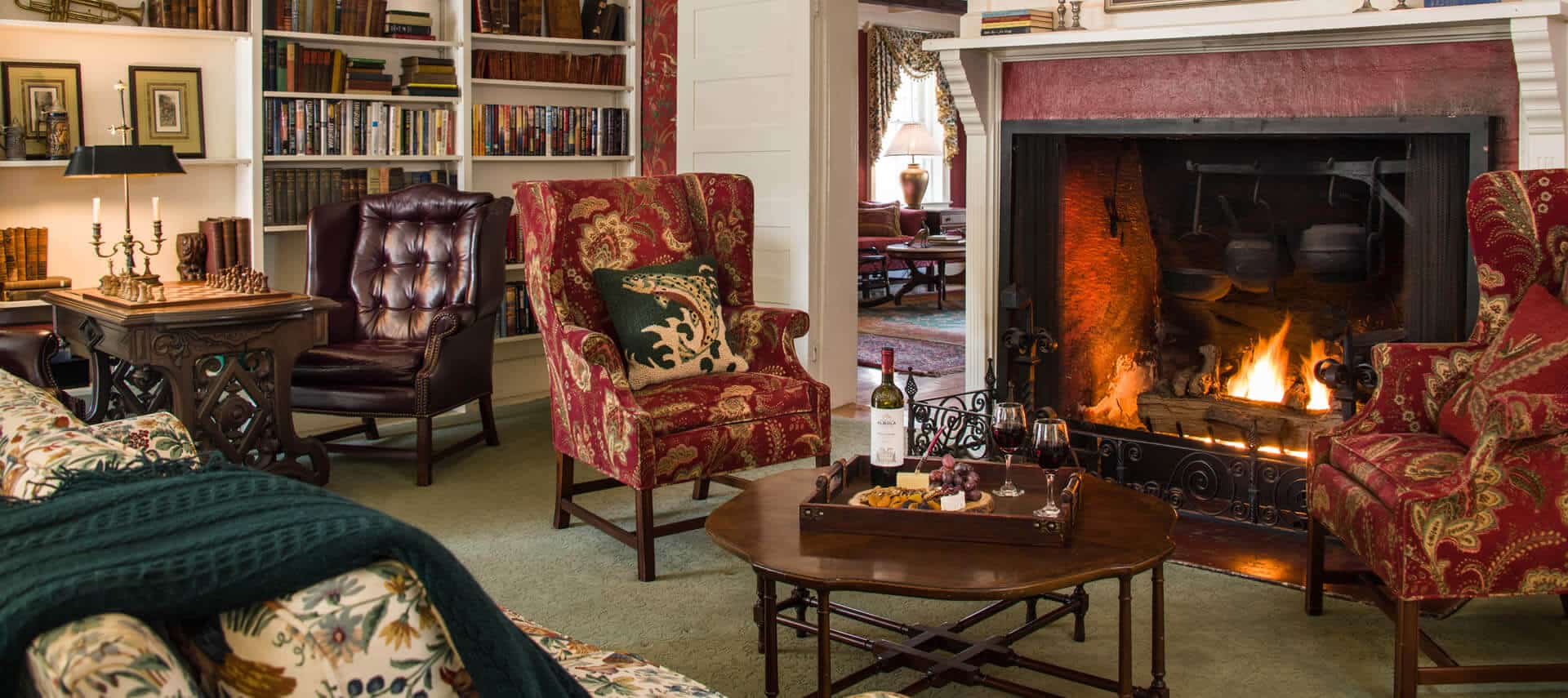 Cozy room with a fireplace, sofa, wingback chairs and a table for games.