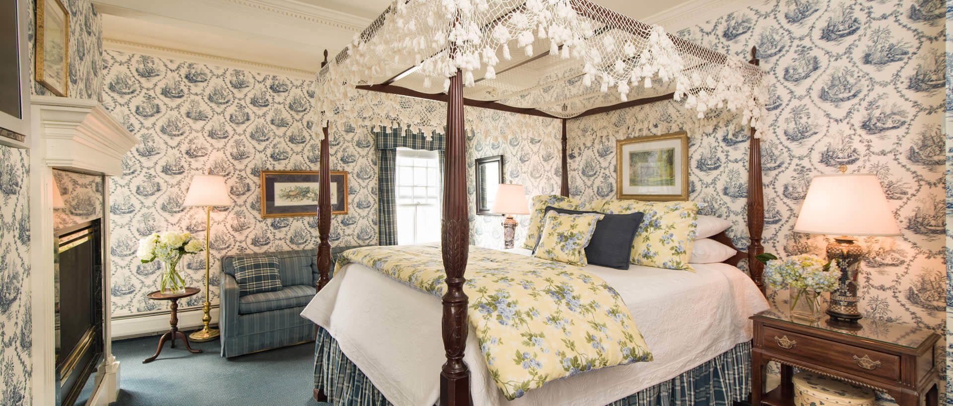 Elegant room with a large canopy bed, blue patterned wallpaper, blue carpets and a fireplace.