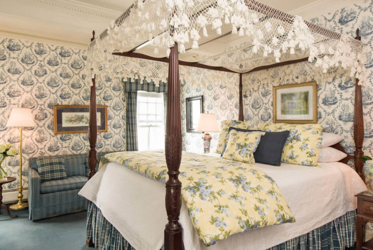 Elegant room with a large canopy bed, blue patterned wallpaper, blue carpets and a fireplace.