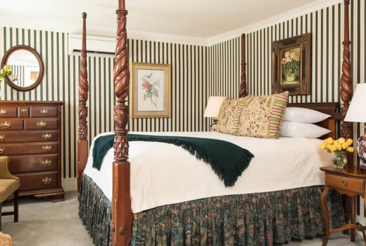 Charming room with a four-post bed, two chairs, green striped wallpaper, and elegant antique wooden furniture.