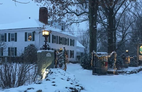 White house with dark shutters and roof in wintertime with gate lit up for the holidays.