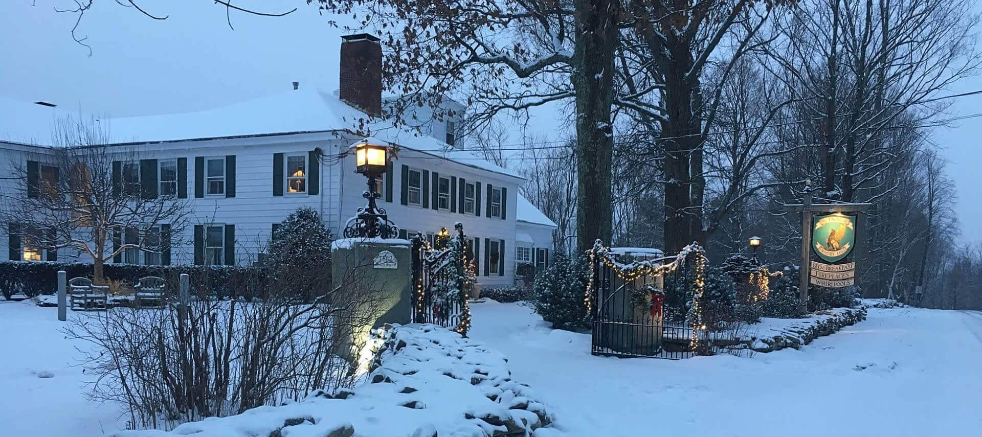 White house with dark shutters and roof in wintertime with gate lit up for the holidays.