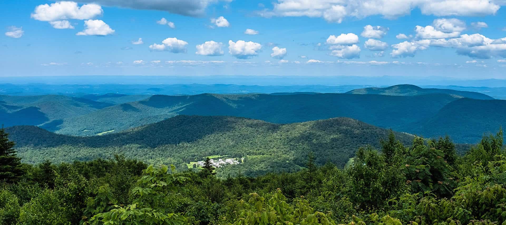 Expansive wide view of tree-covered rolling hills and blue sky with a building right in the middle of it.